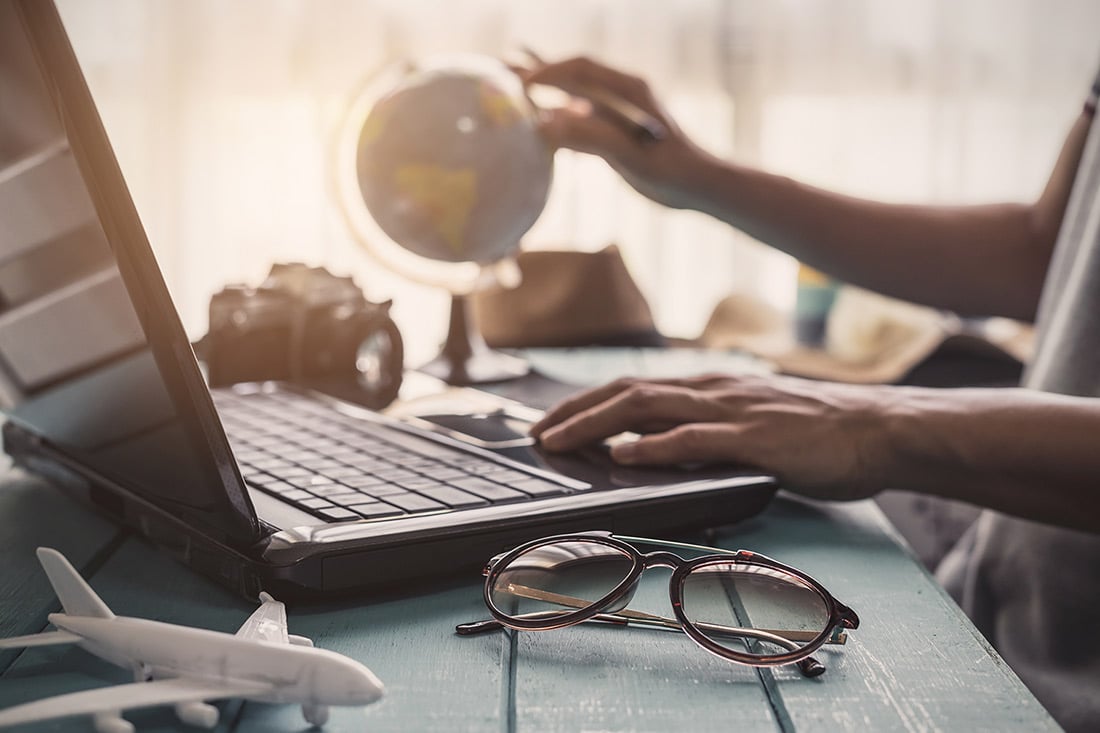Traveler on laptop plotting on a desk globe