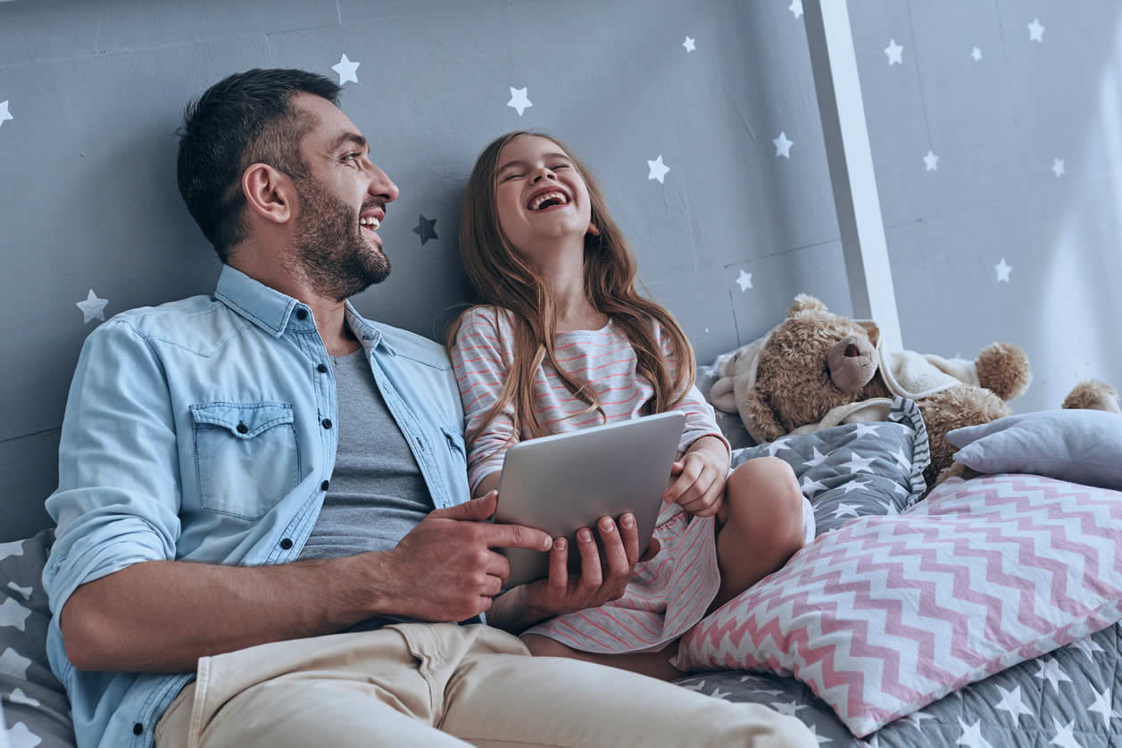 Father and daughter sat on bed laughing