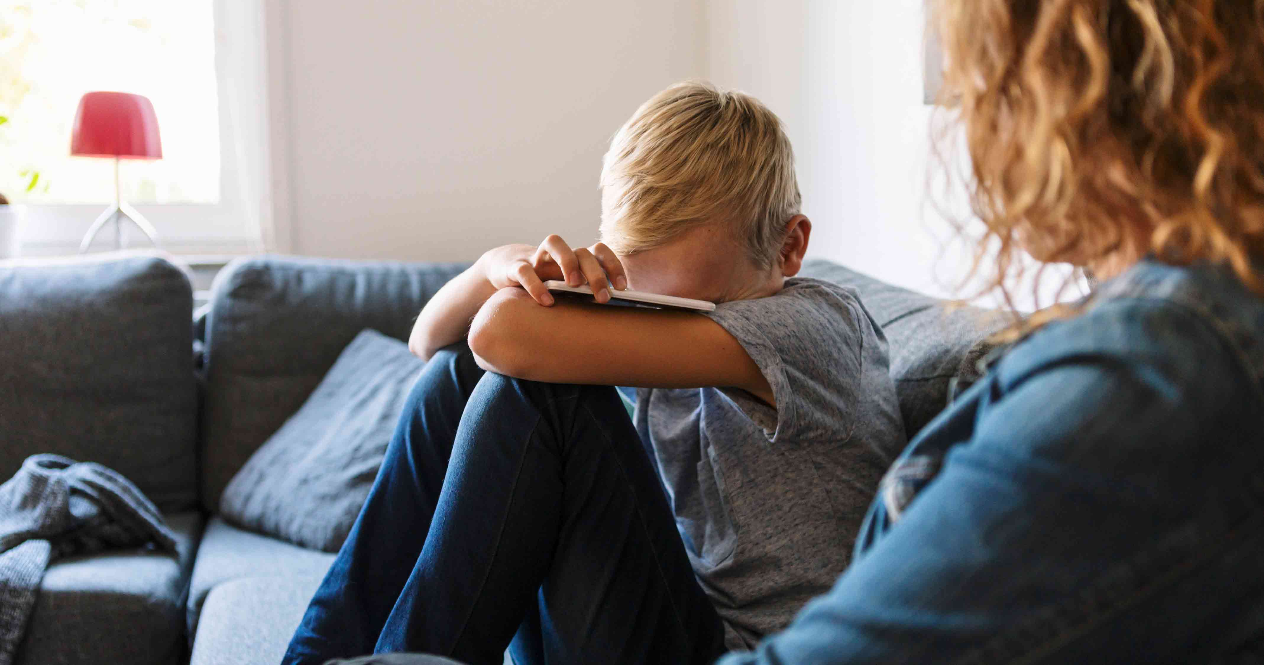 sad boy sitting on couch with mother