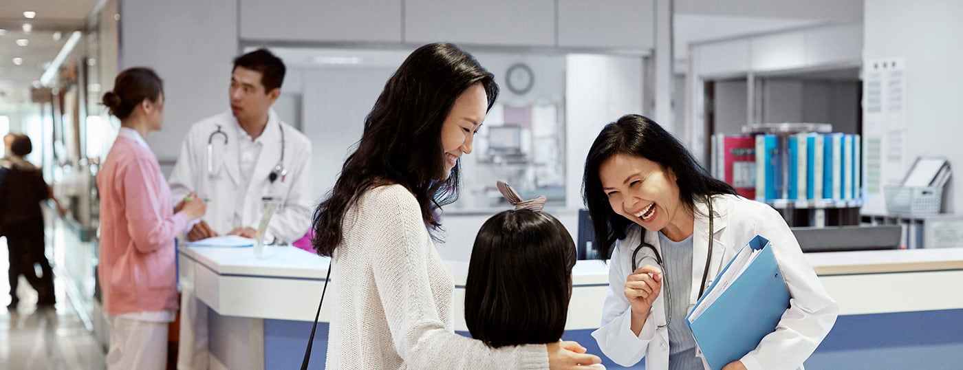 Smiling doctor chatting to mother and daughter at hospital reception