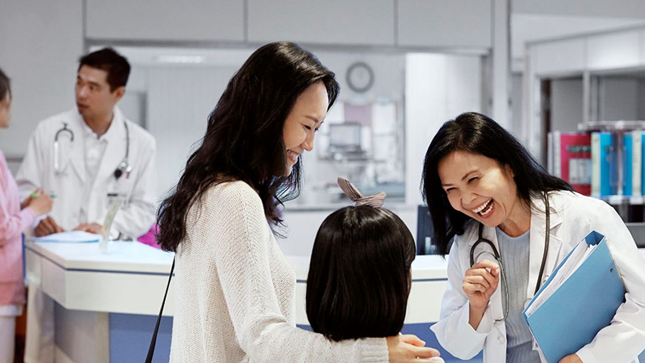 Smiling doctor chatting to mother and daughter at hospital reception