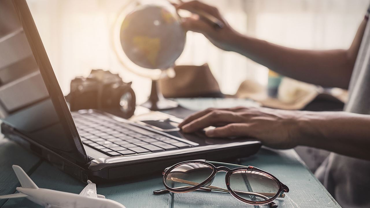 Traveler looking at laptop and plotting on a globe
