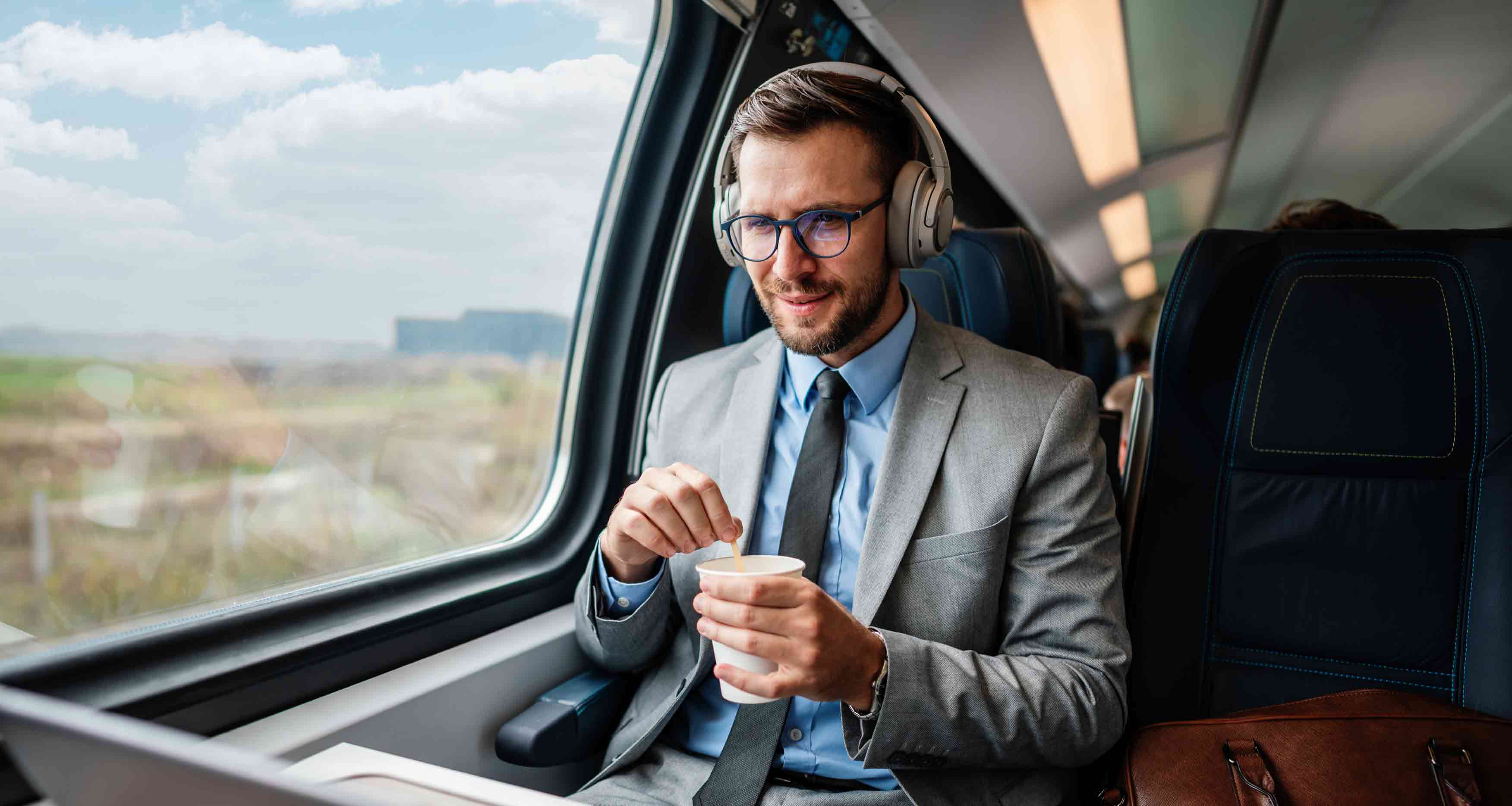 businessman-with-glasses-and-headphones-sitting-on-the-train-looking-at-laptop