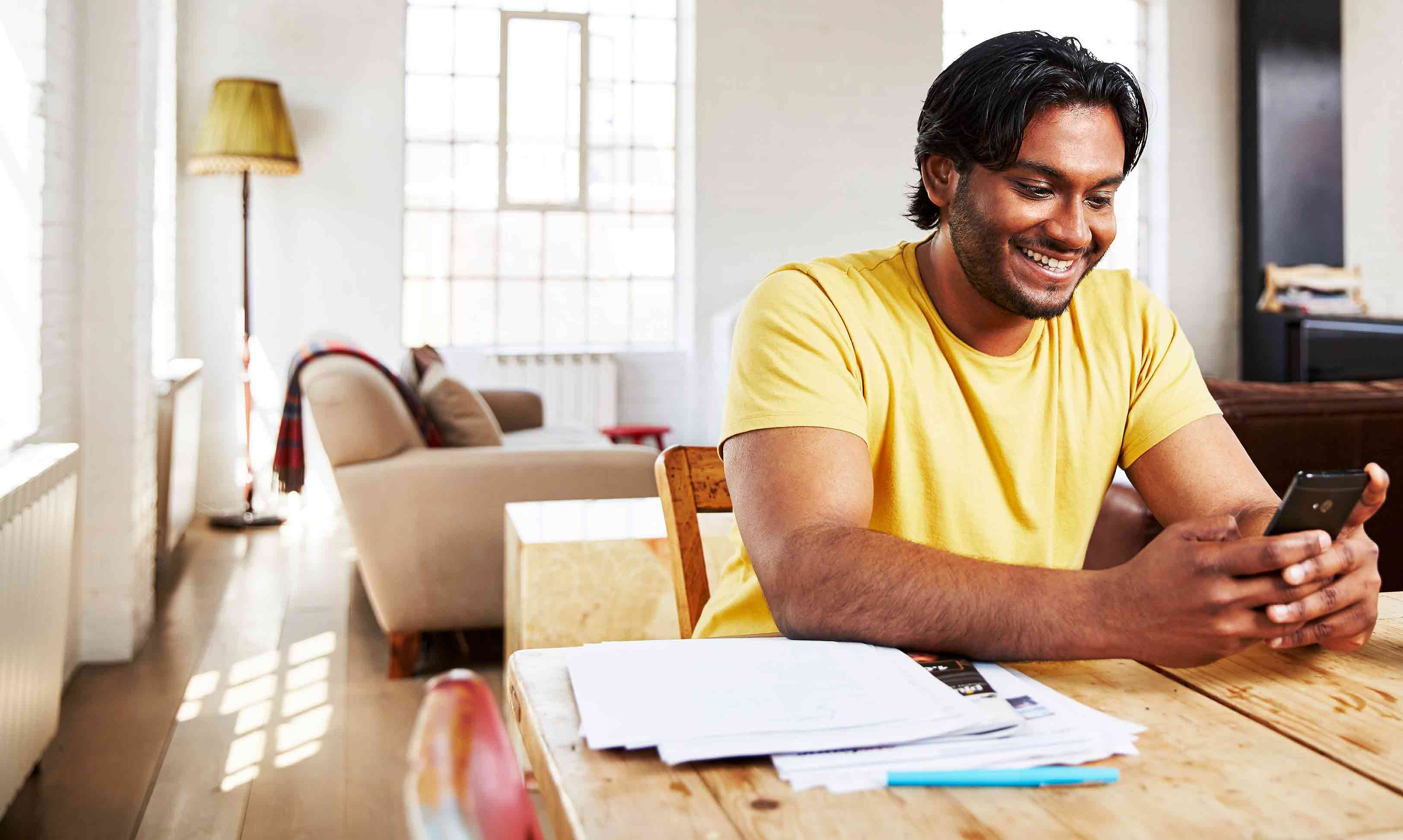 Man-smiling-at-phone-sitting-at-wooden-table