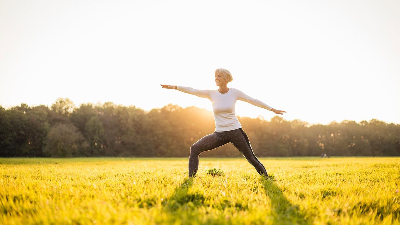 Older woman holding warrior yoga pose in field