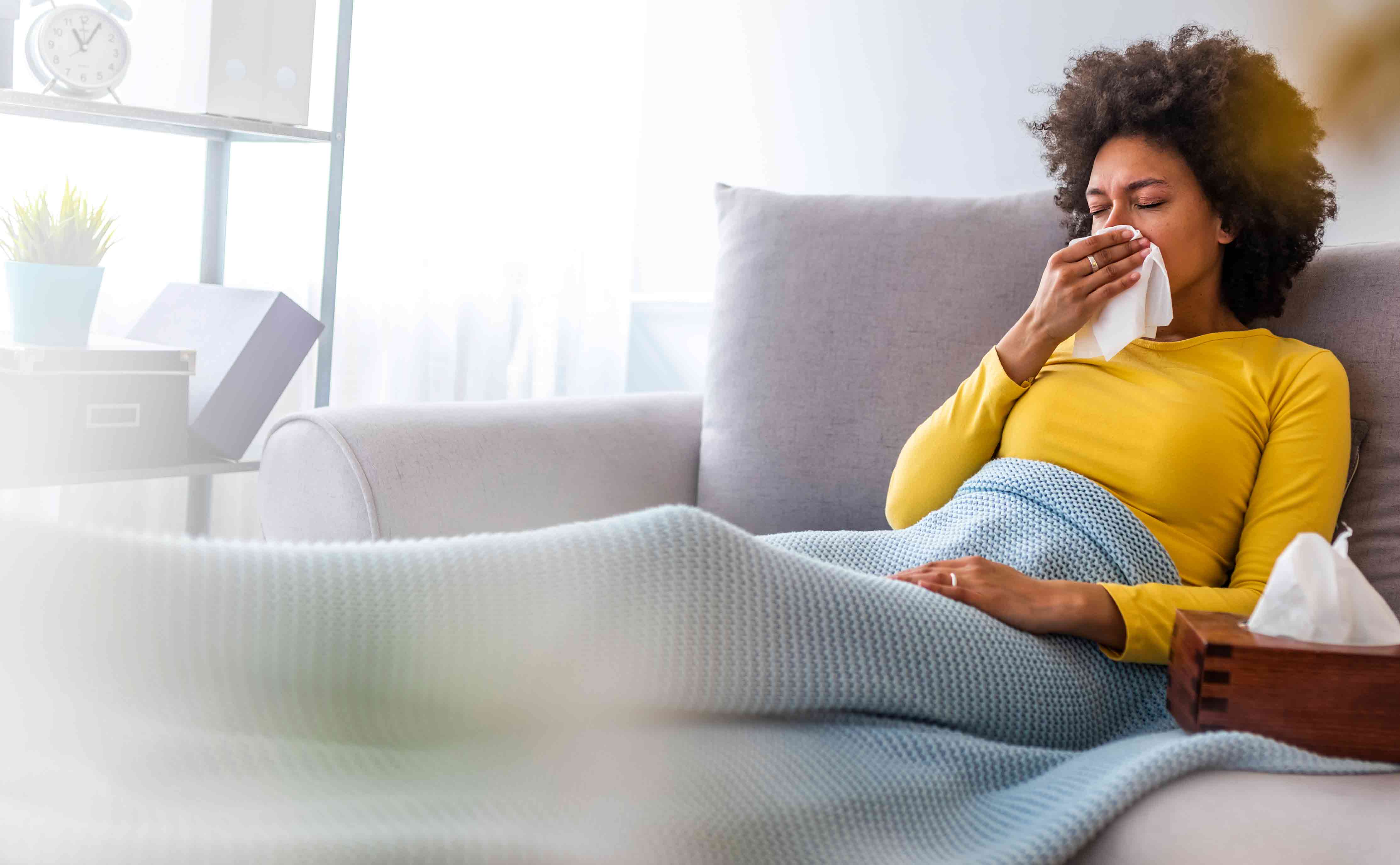 Sick-woman-sitting-on-couch-blowing-nose