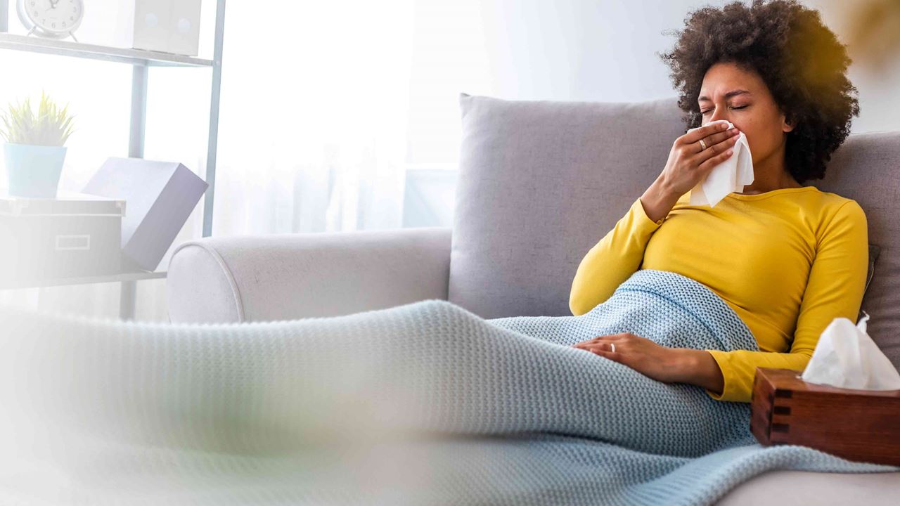 Sick-woman-sitting-on-couch-blowing-nose