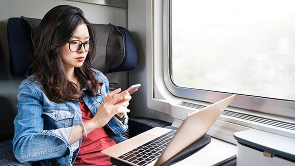 Woman on train using phone and laptop.