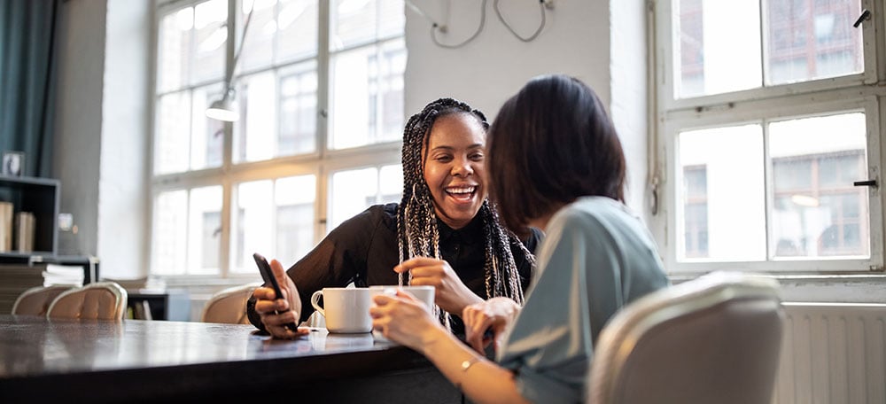 two women smiling at each other in a coffee shop
