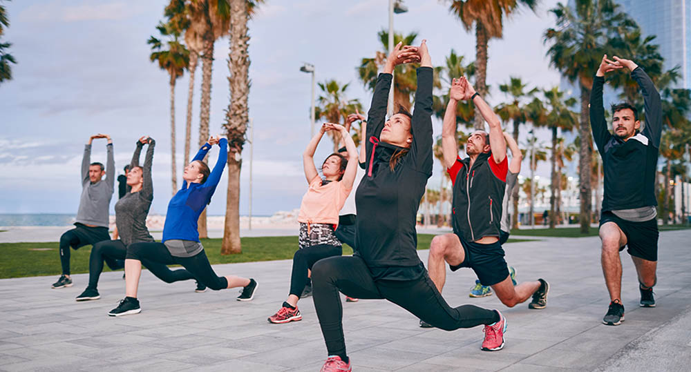 group of people doing yoga on a boardwalk in front of palm trees