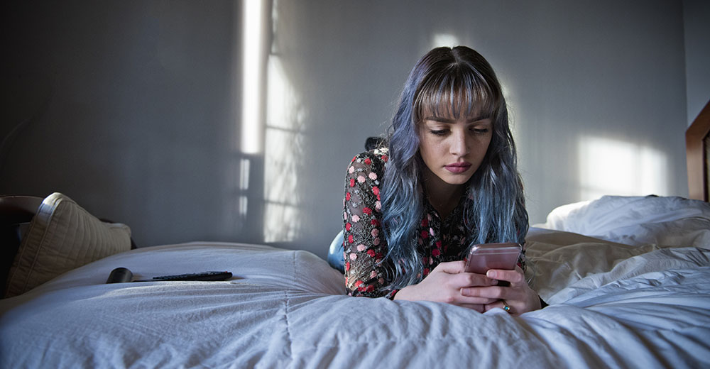 Teenage girl lying on bed looking at phone