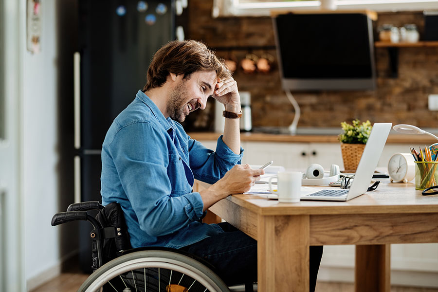 Man in wheelchair at table looking at phone and laptop