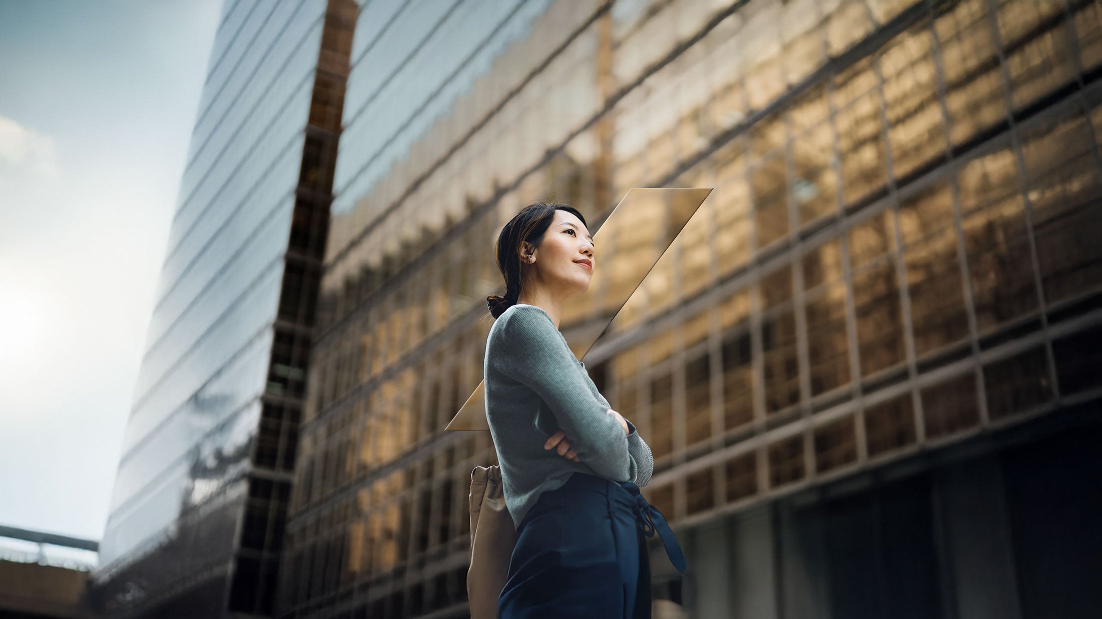 Low angle portrait of confident and successful young Asian businesswoman standing against contemporary corporate skyscrapers in financial district.