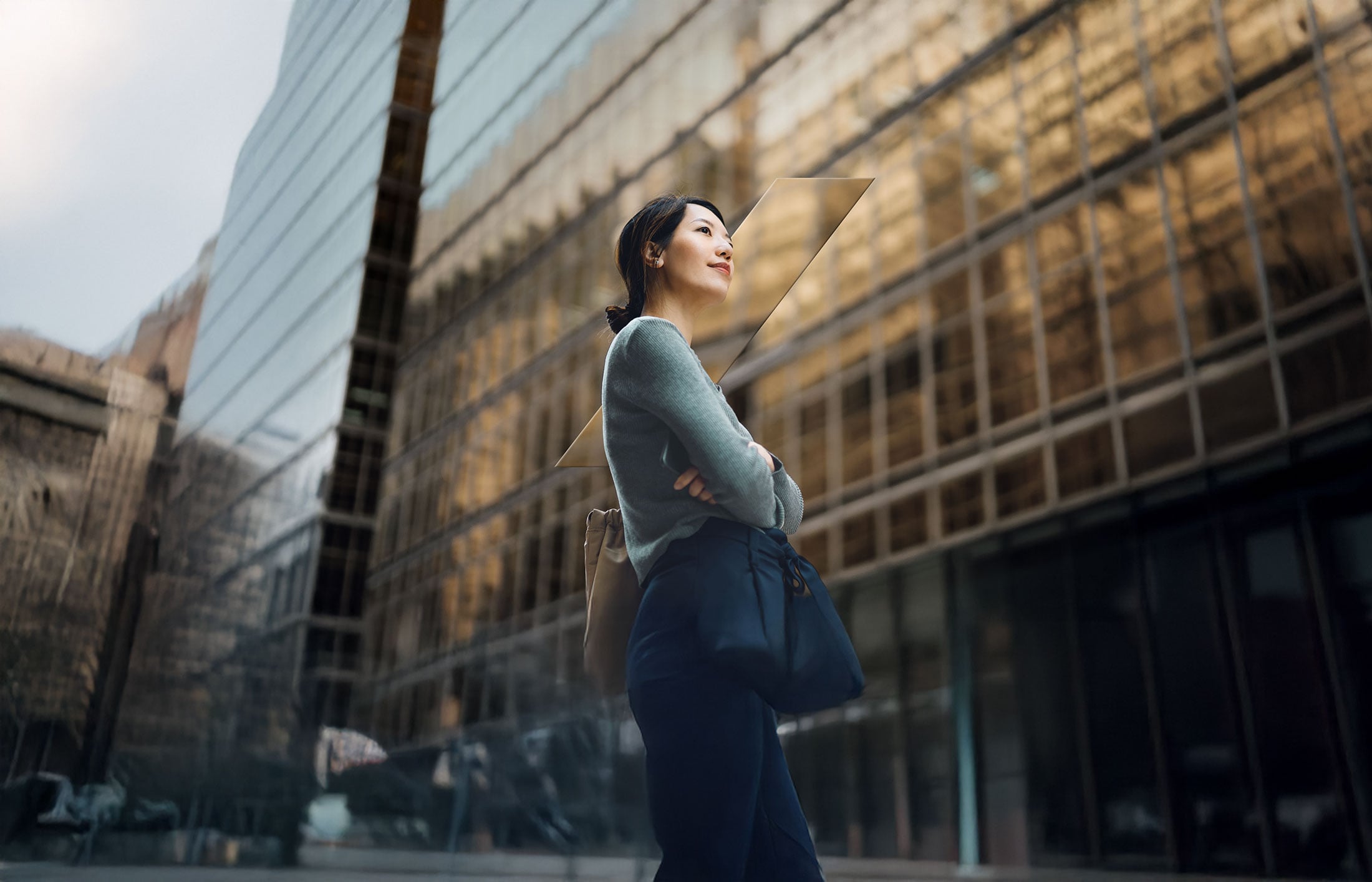 Low angle portrait of confident and successful young Asian businesswoman standing against contemporary corporate skyscrapers in financial district.