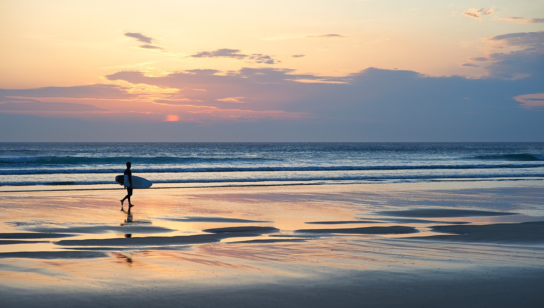 Surfer walking along beach at dusk