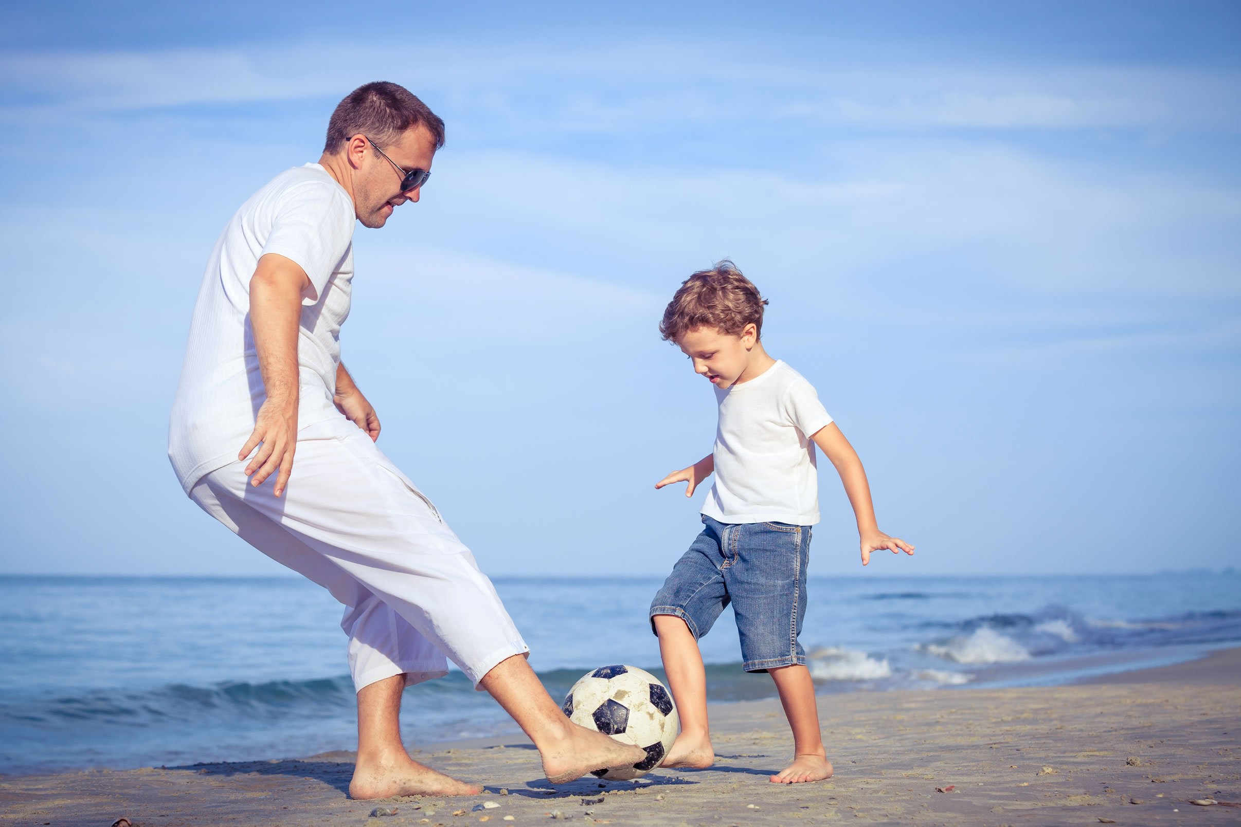 Father and son playing football on the beach