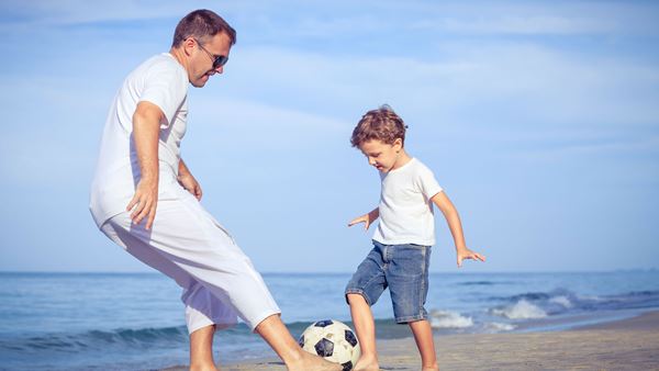Father and son playing football on the beach