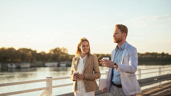Woman and man walking by river drinking coffee