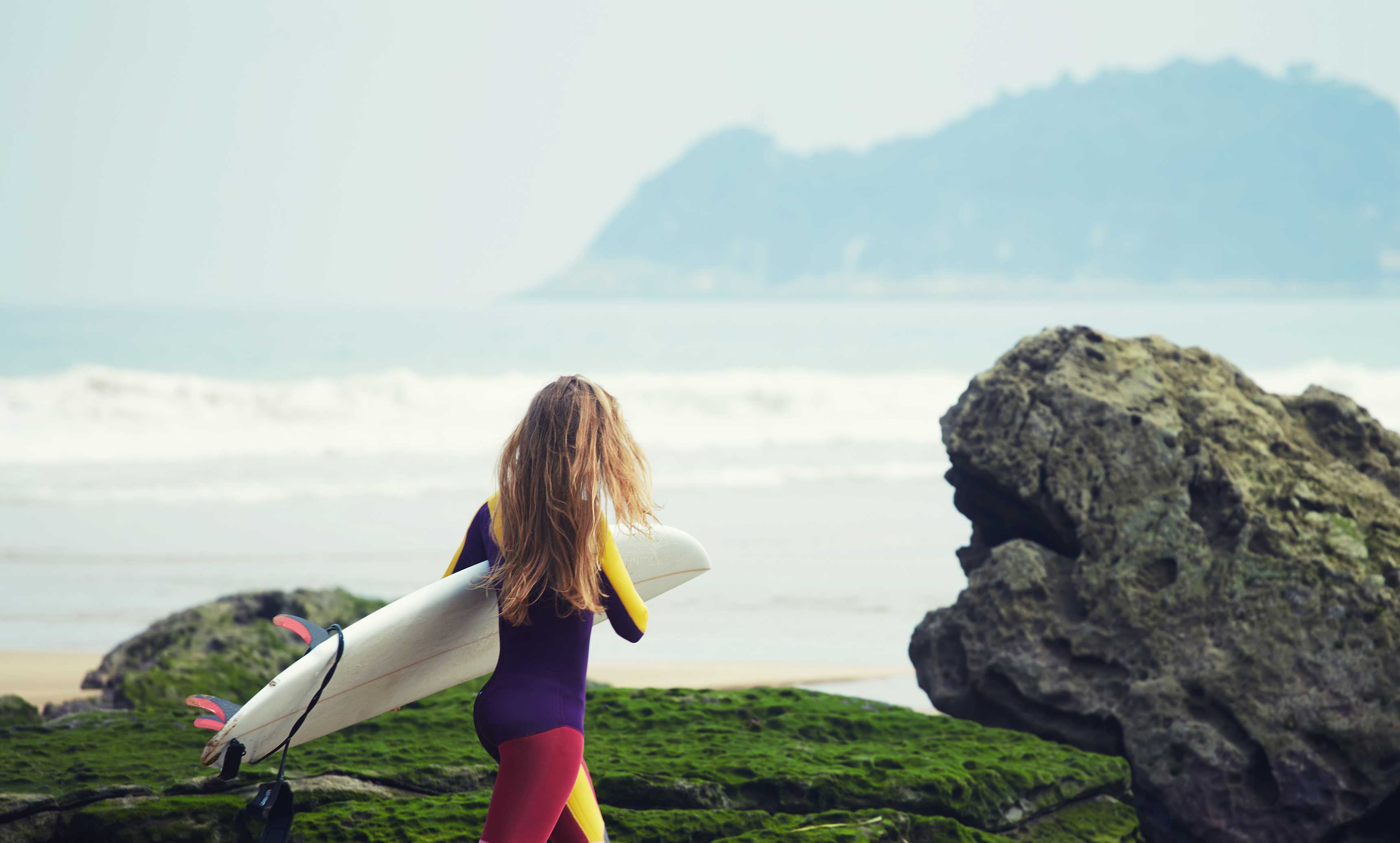 young woman with surfboard by the rocky coast