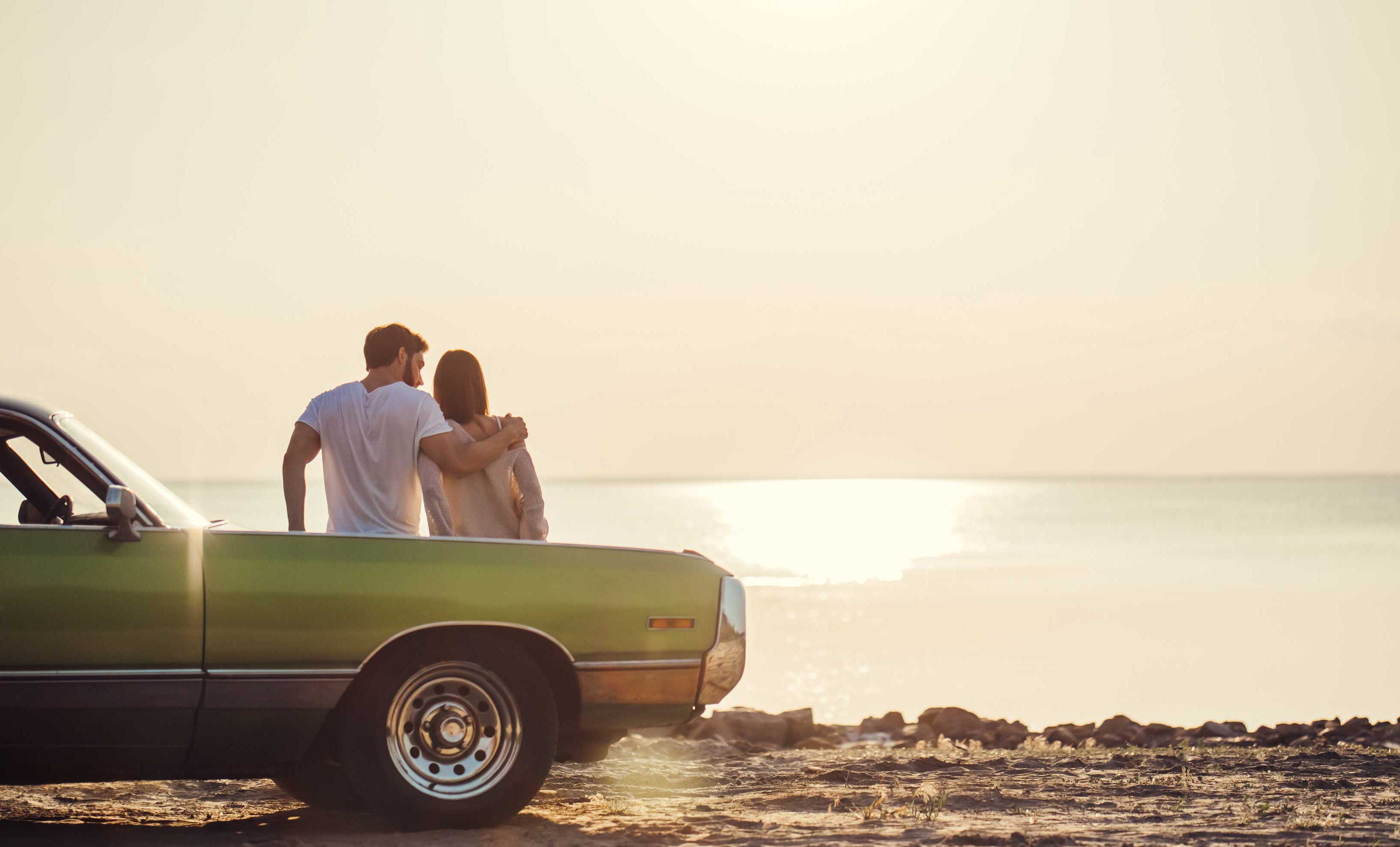 young couple leaning on car watching the sunset