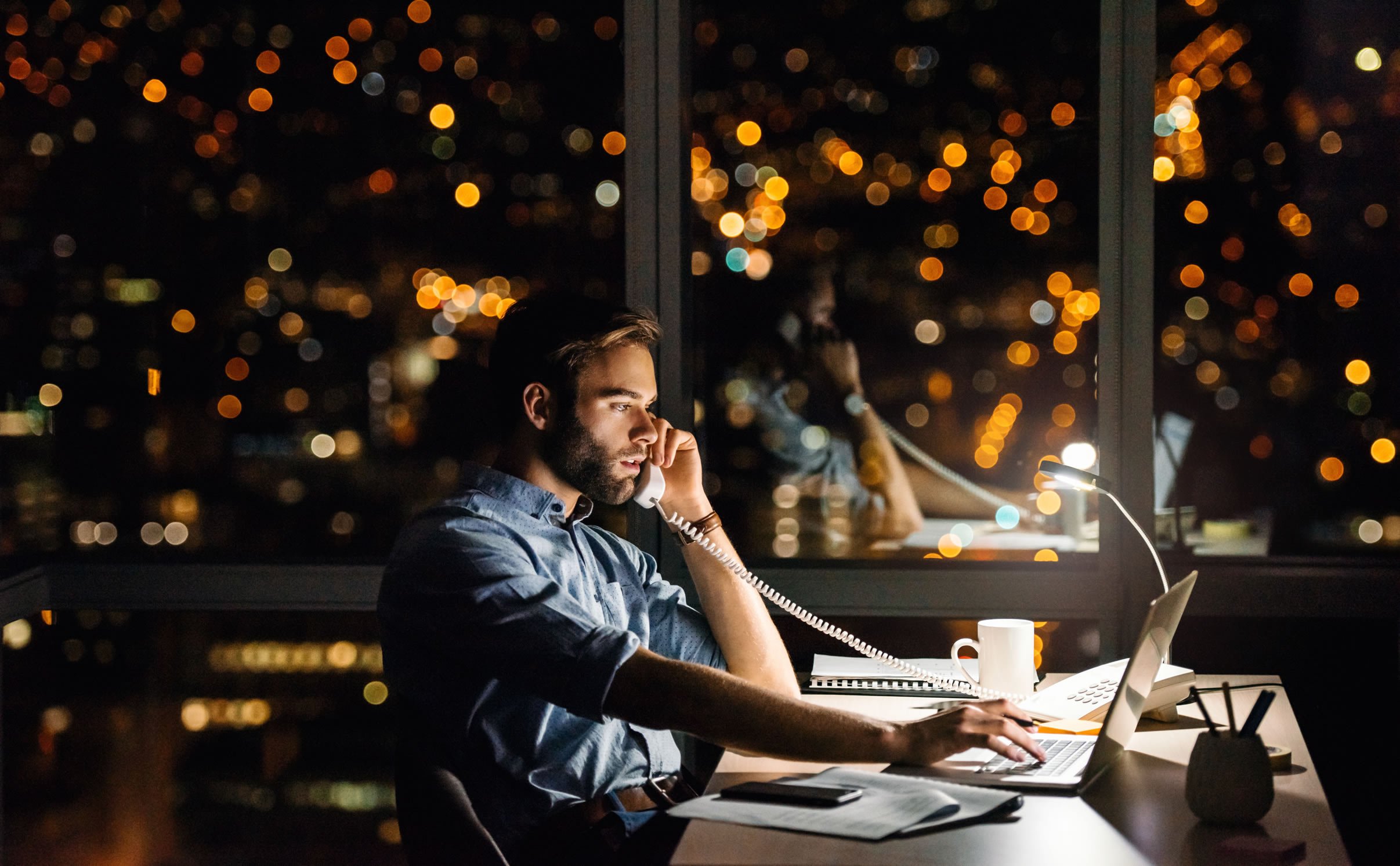 Man on phone in office with evening city view