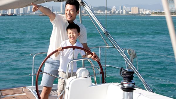 Father and son smiling and sailing on a yacht