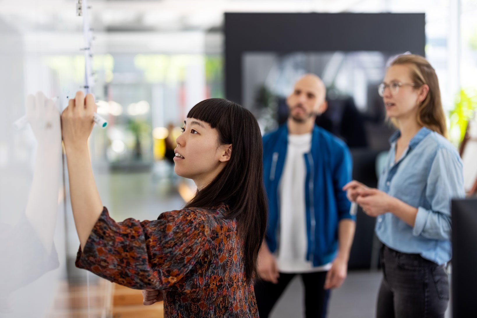 A young woman writing on a whiteboard for her colleagues