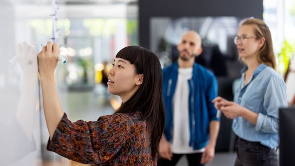A young woman writing on a whiteboard for her colleagues