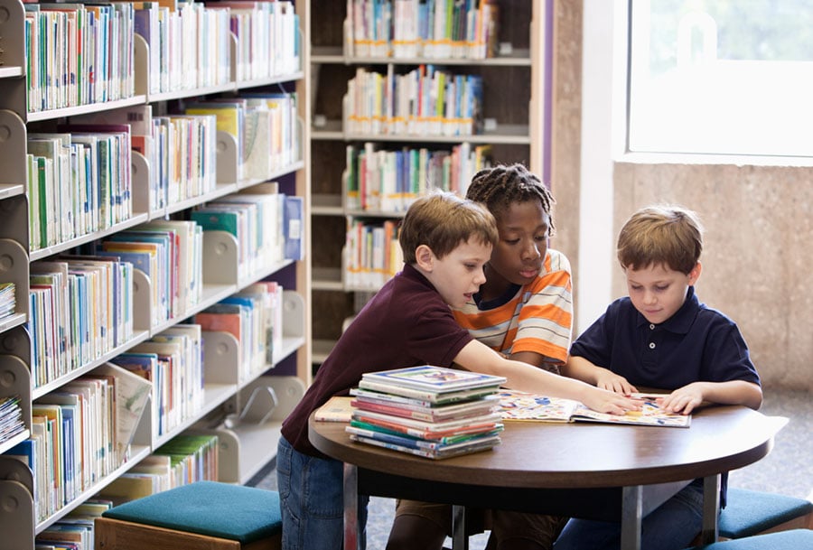 three young boys sitting in a library reading together