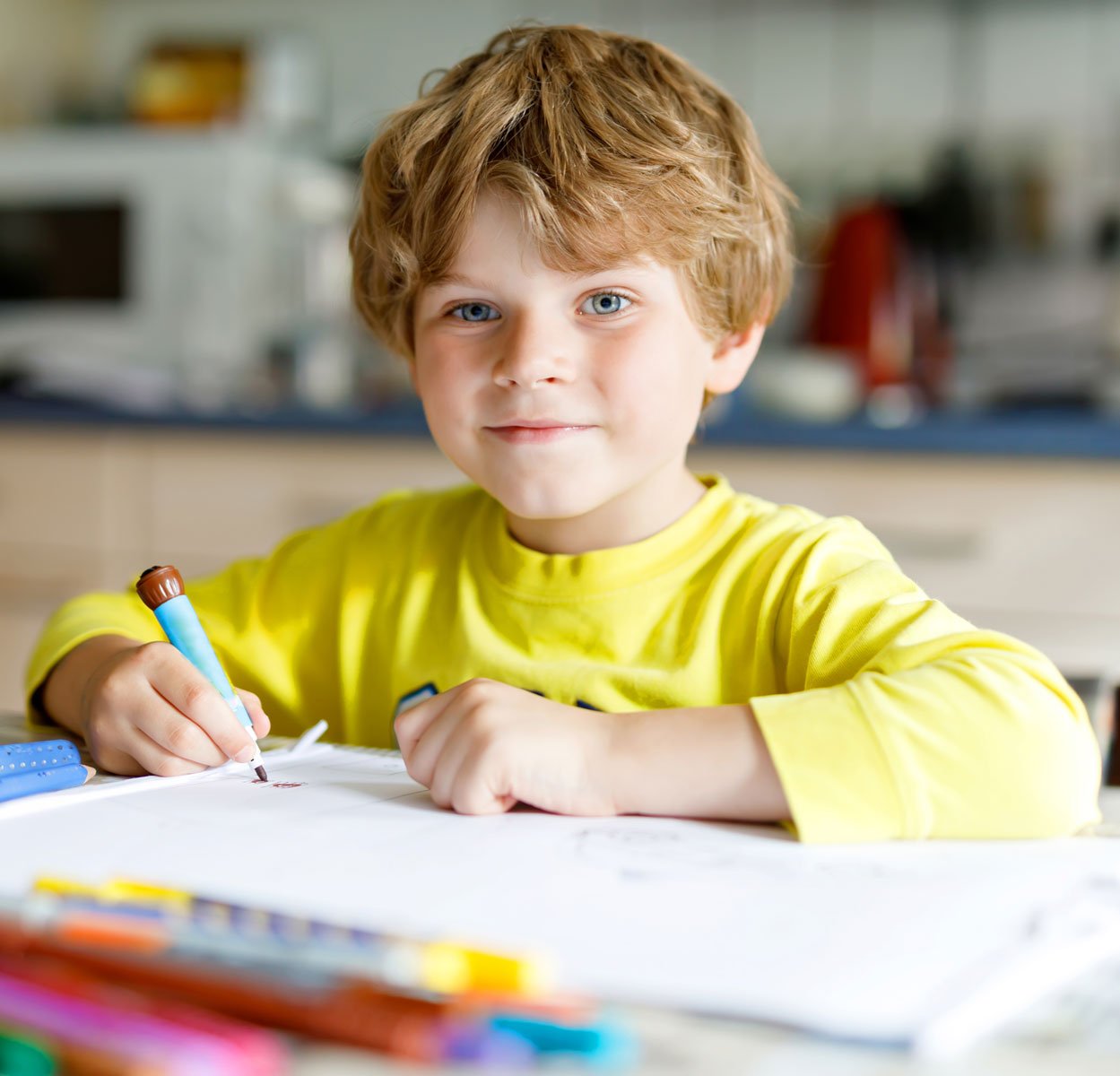 young smiling boy in yellow shirt drawing