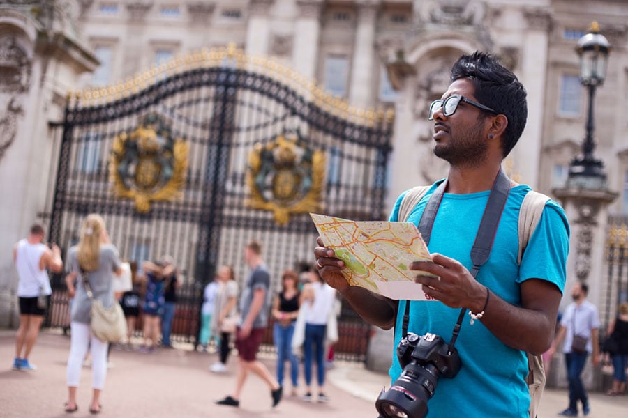 bespectacled man consulting map in front of buckingham palace gates