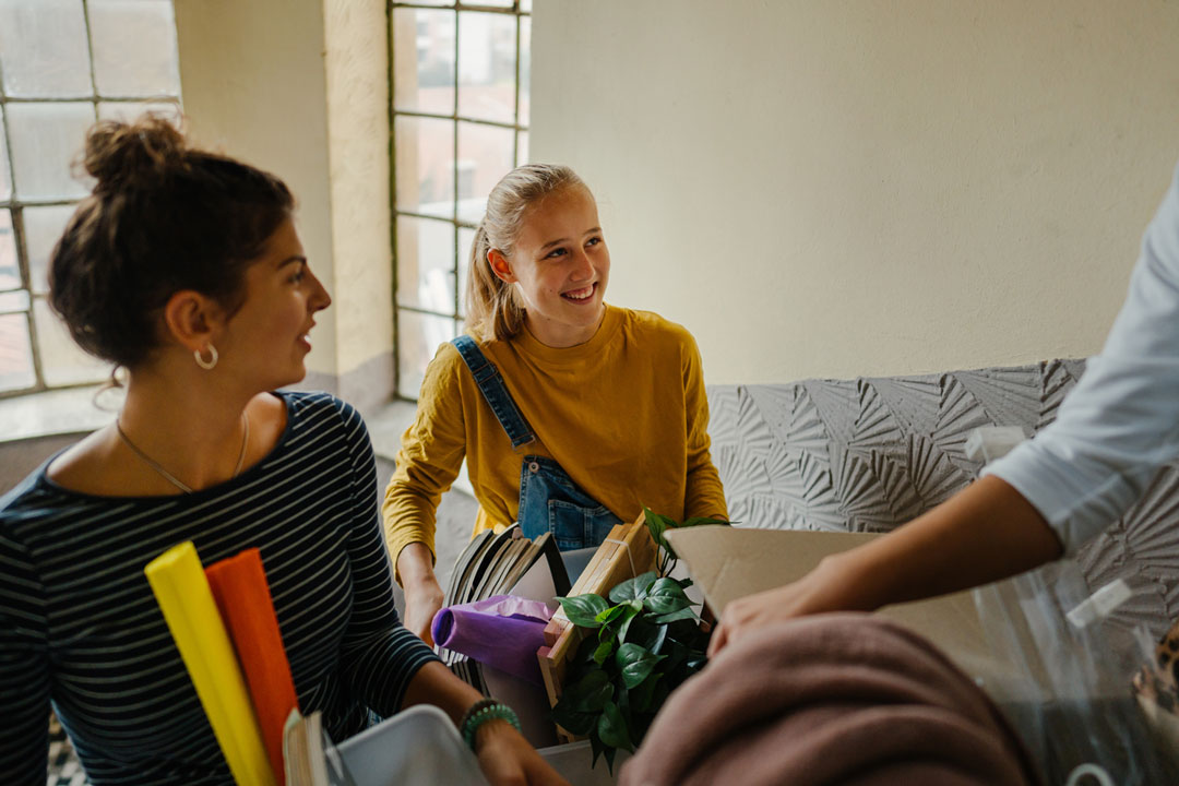 young woman smiling as she carries boxes into her new apartment